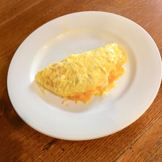 An omelet on a white serving plate resting on a wooden surface