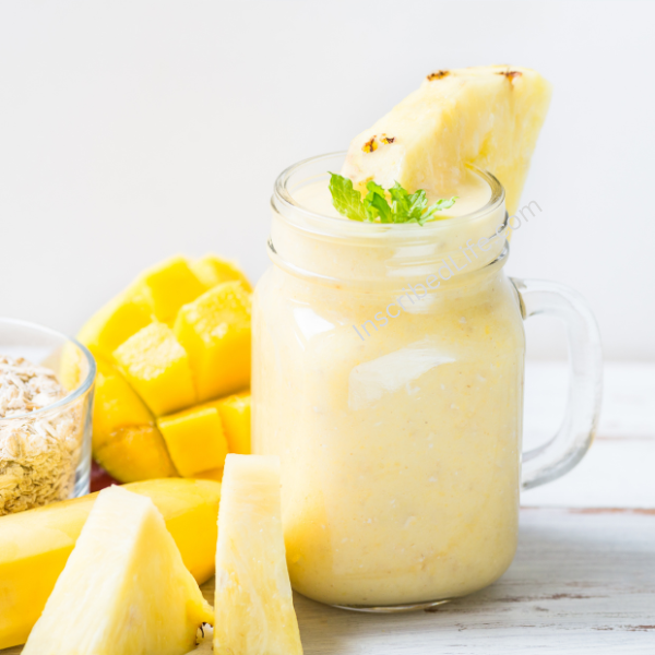 A pineapple smoothie in a MASON Jar with a pineapple slice on it and pineapples around it