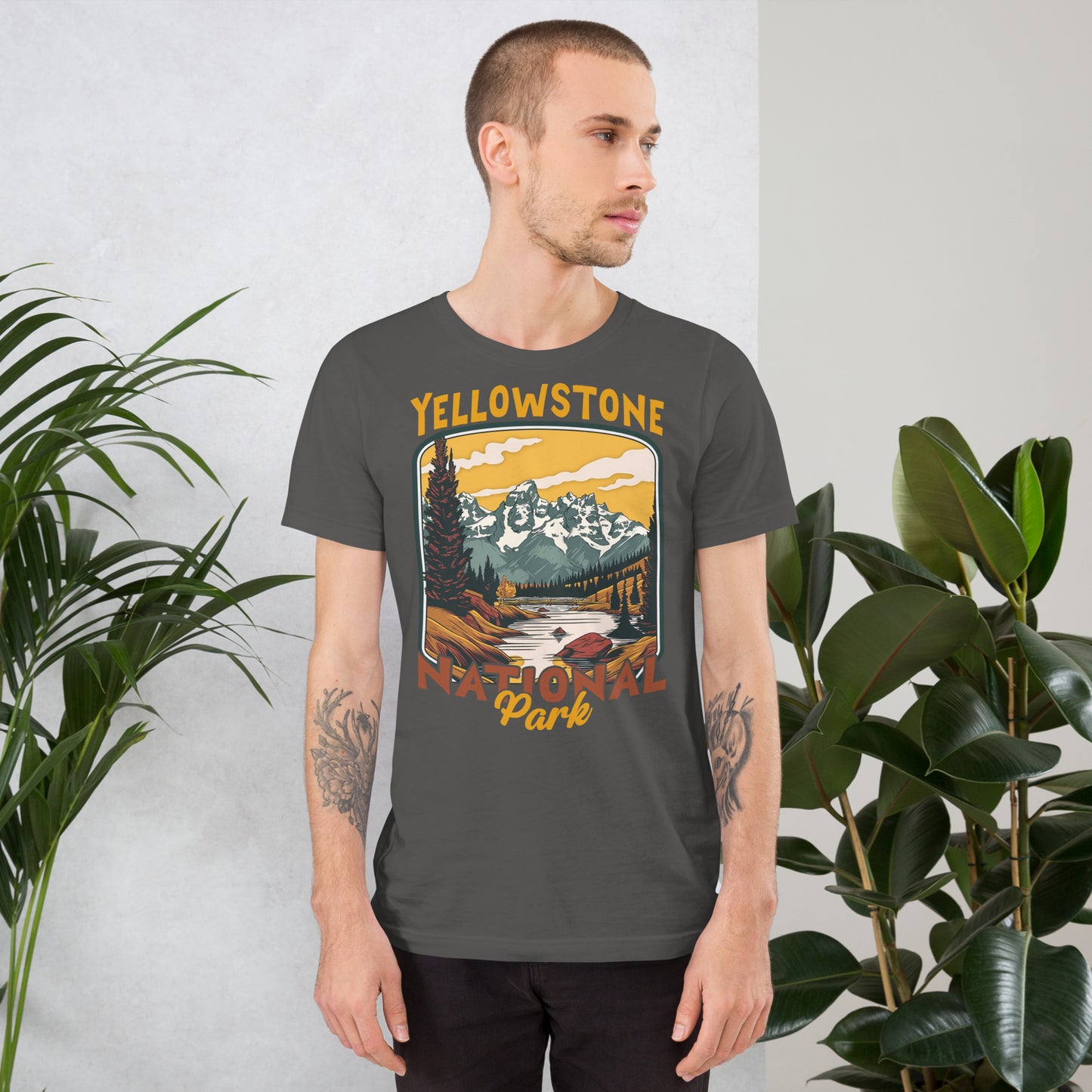 A male with head to the right wearing the Yellowstone National Park T-shirt in asphalt gray against a wall with flowers