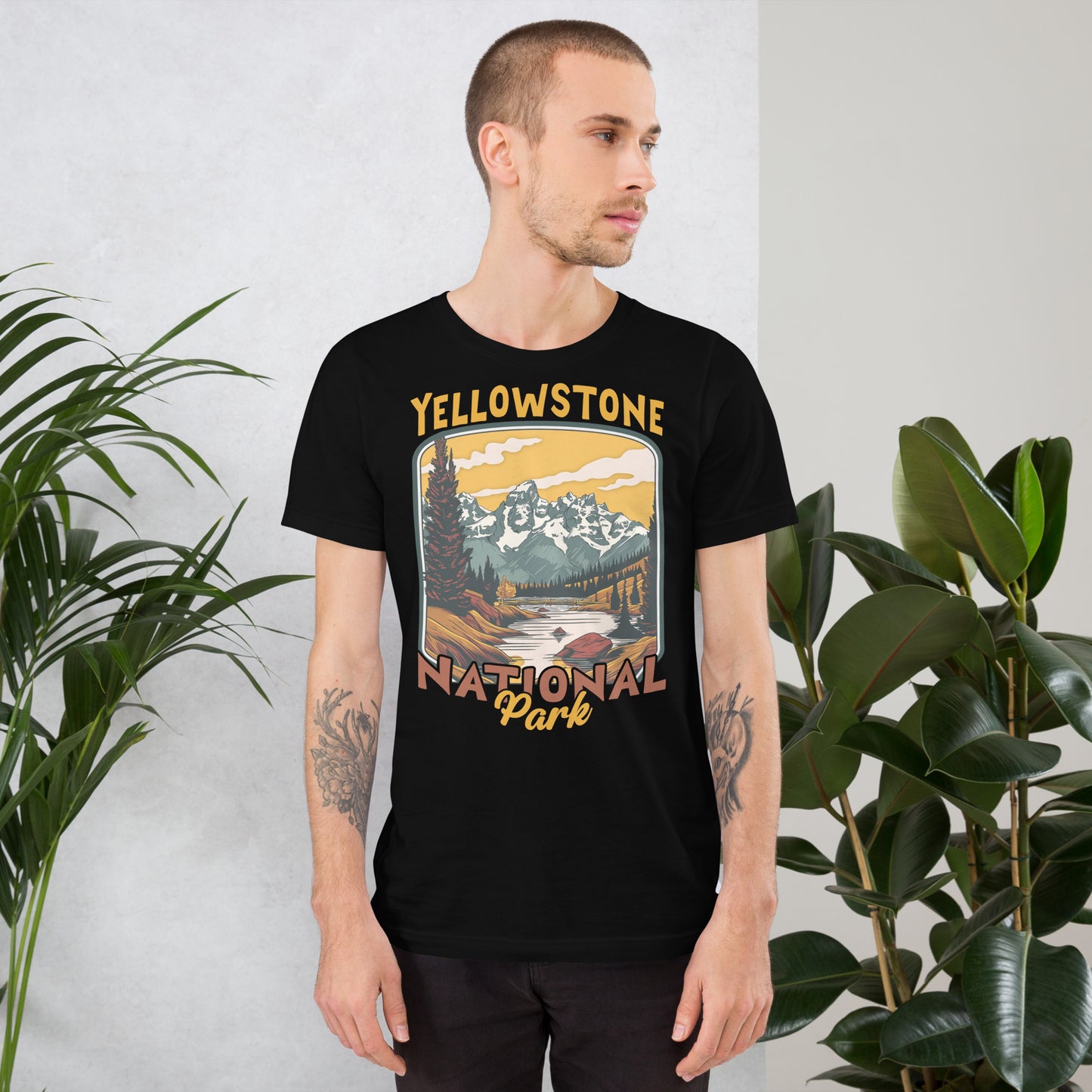 A male with head to the right wearing the Yellowstone National Park T-shirt in black against a wall with flowers