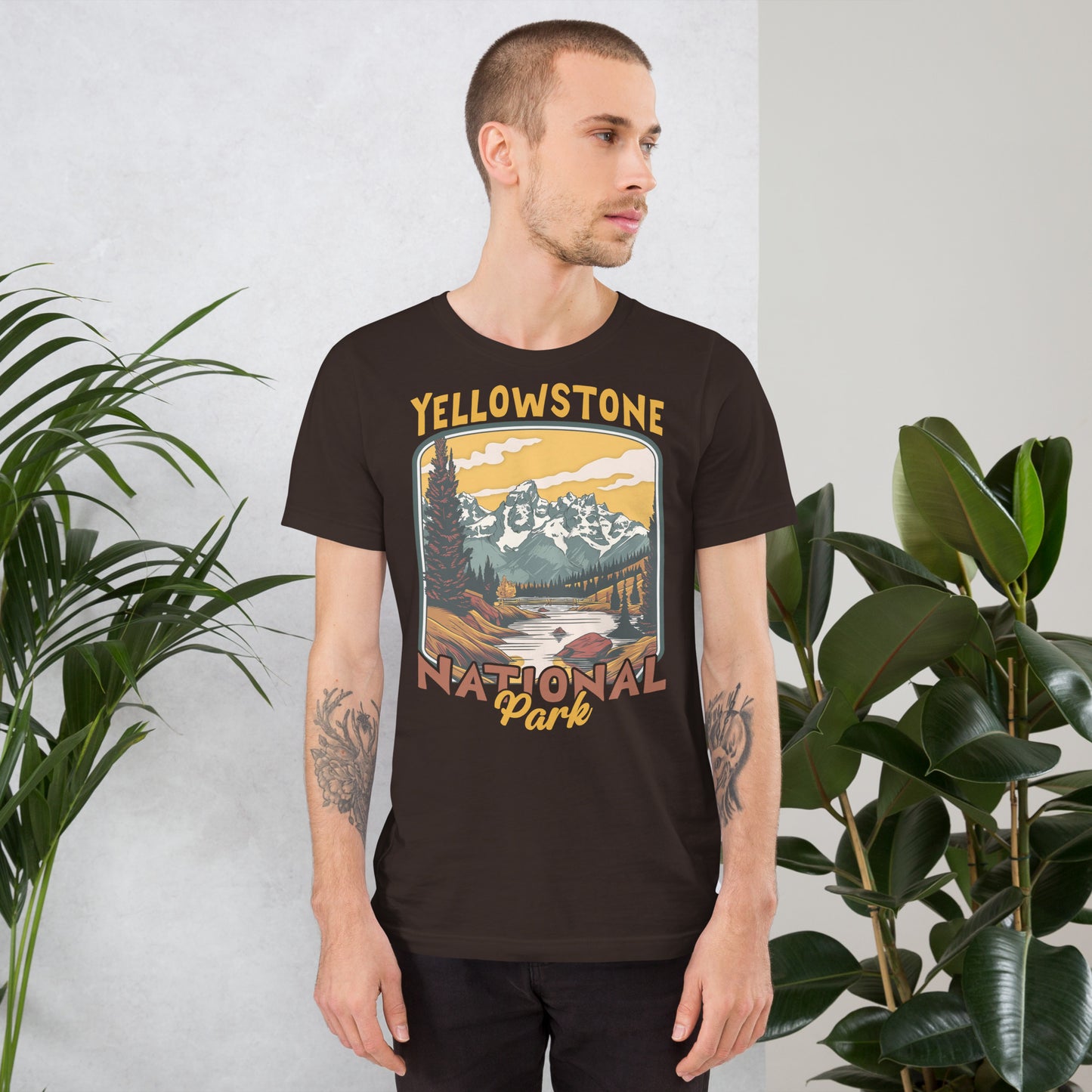 A male with head to the right wearing the Yellowstone National Park T-shirt in brown against a wall with flowers