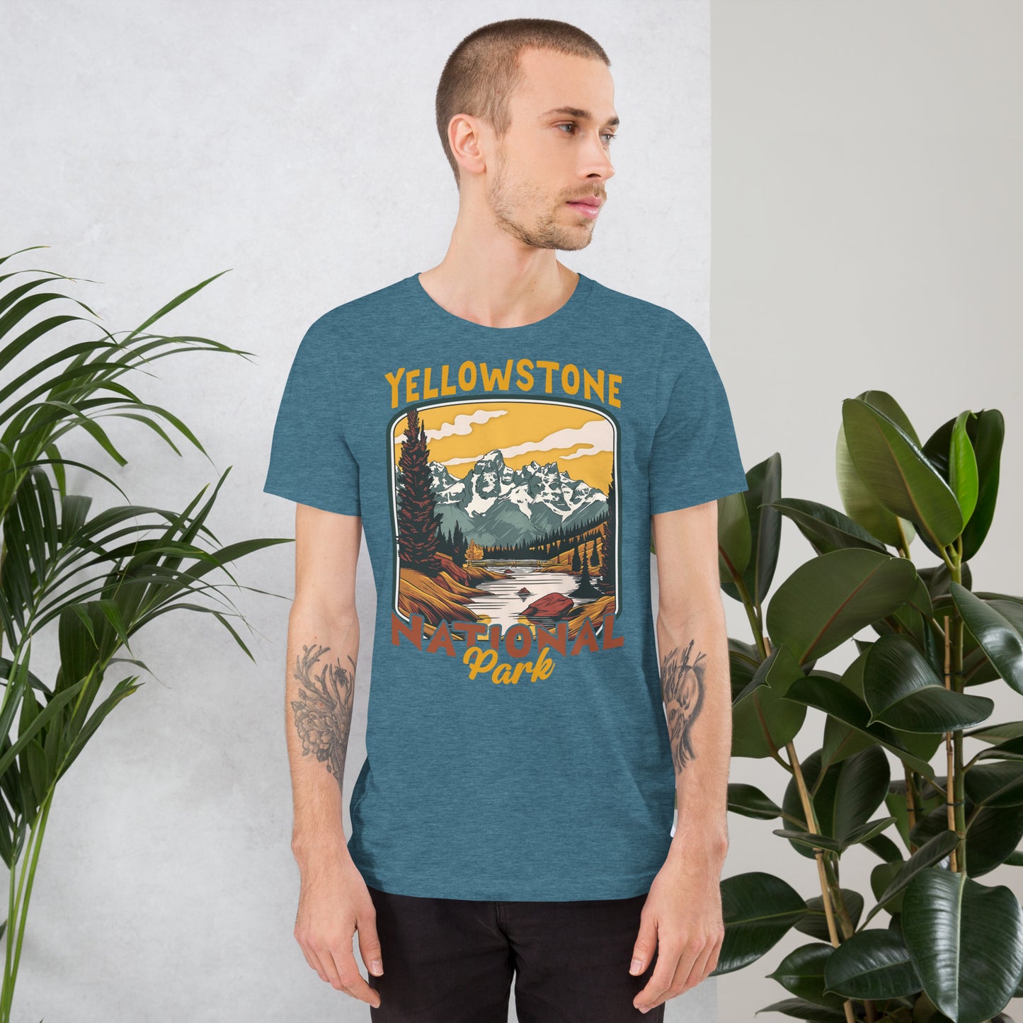 A male with head to the right wearing the Yellowstone National Park T-shirt in heather deep teal against a wall with flowers