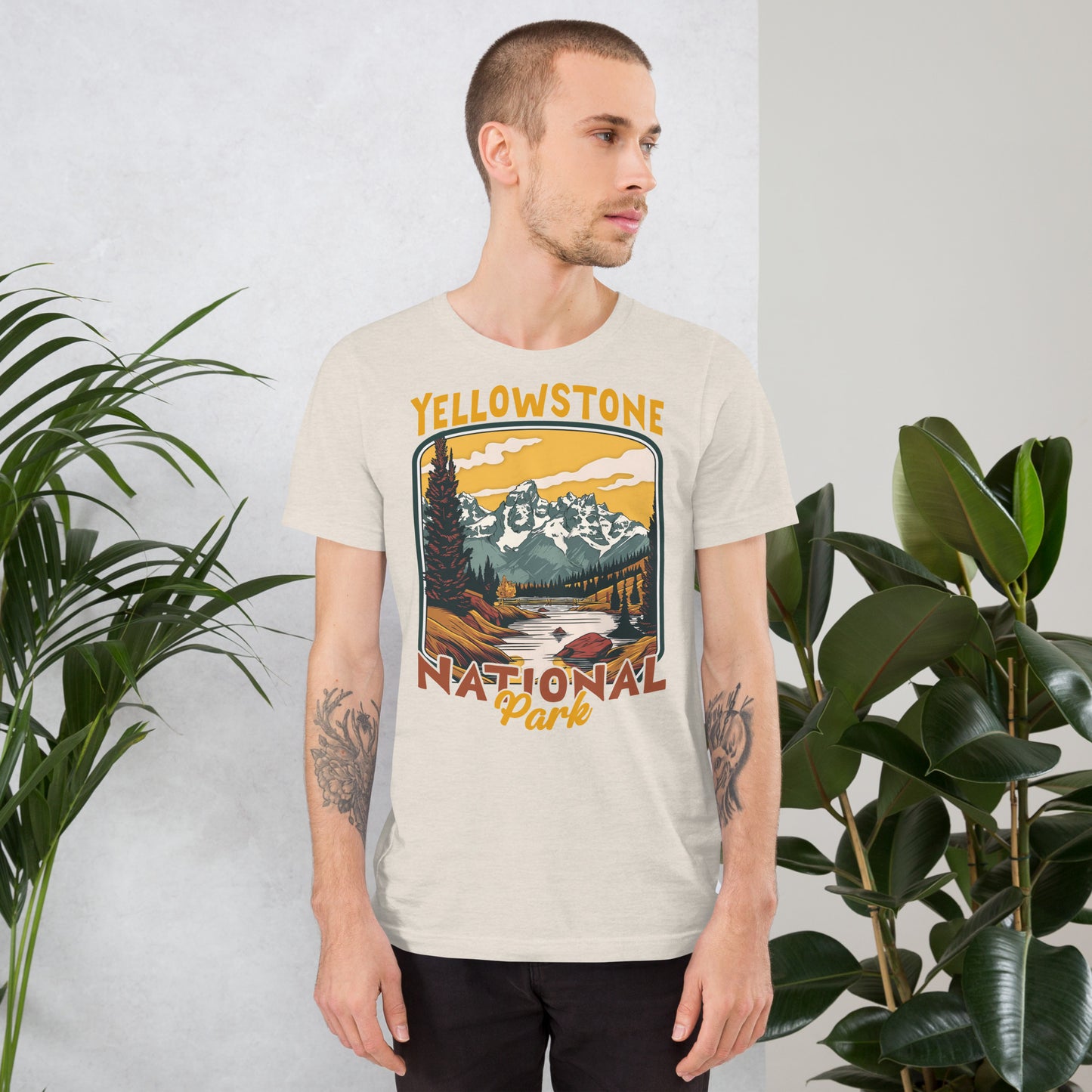 A male with head to the right wearing the Yellowstone National Park T-shirt in heather dust against a wall with flowers