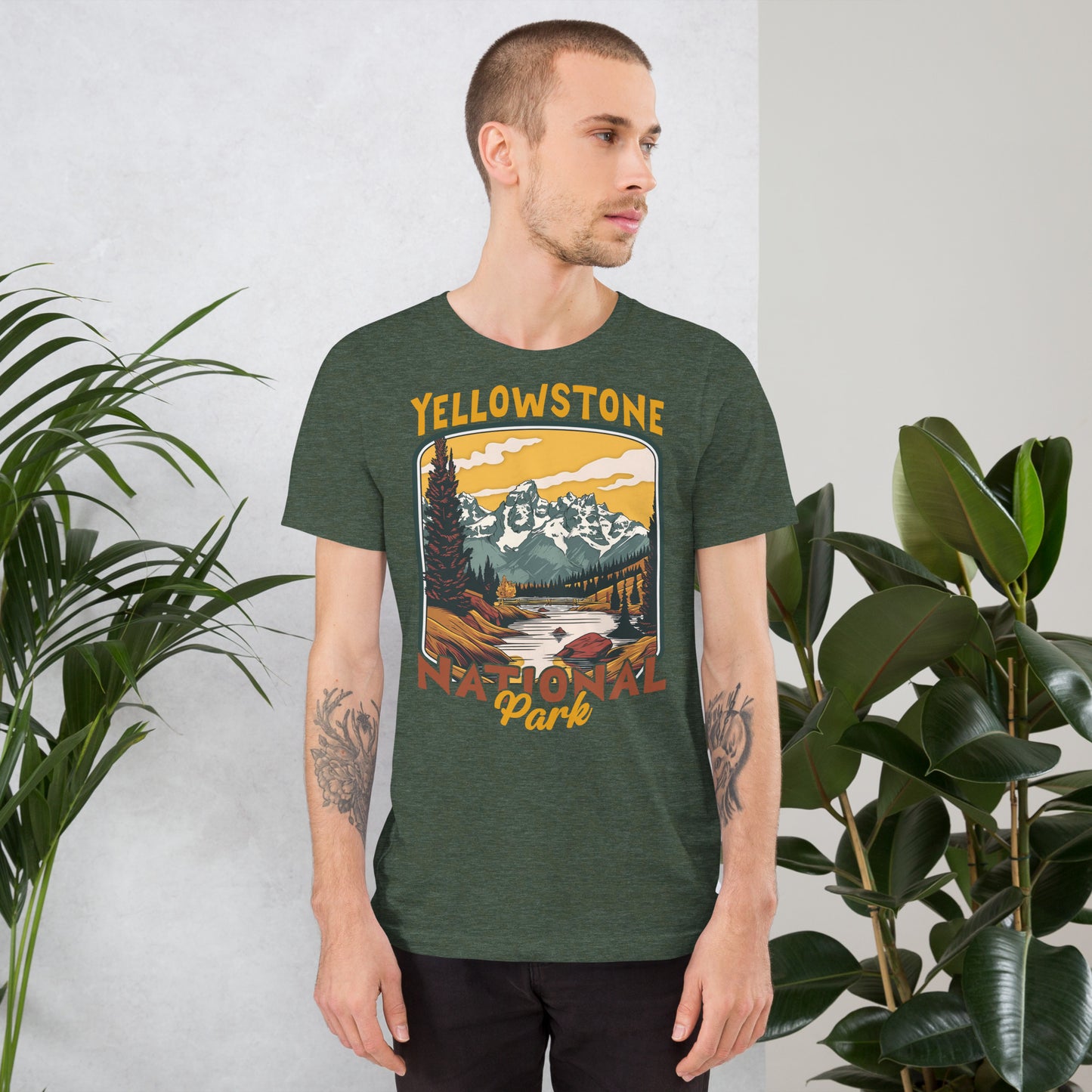 A male with head to the right wearing the Yellowstone National Park T-shirt in heather forest green against a wall with flowers