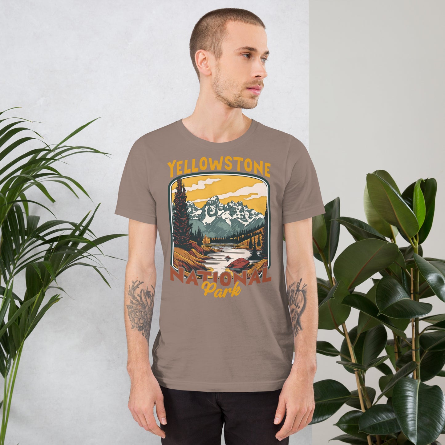 A male with head to the right wearing the Yellowstone National Park T-shirt in pebble against a wall with flowers