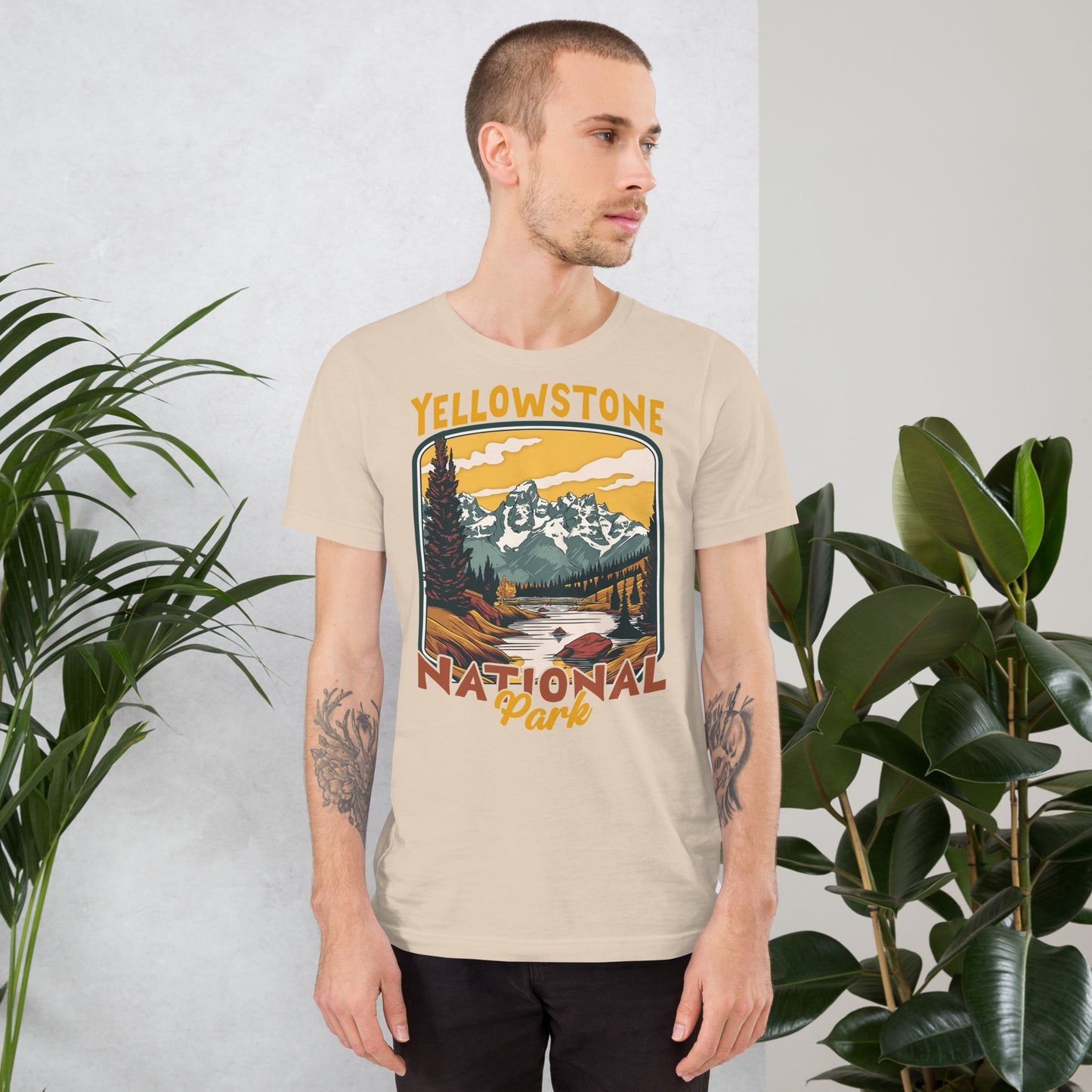 A male with head to the right wearing the Yellowstone National Park T-shirt in soft cream against a wall with flowers