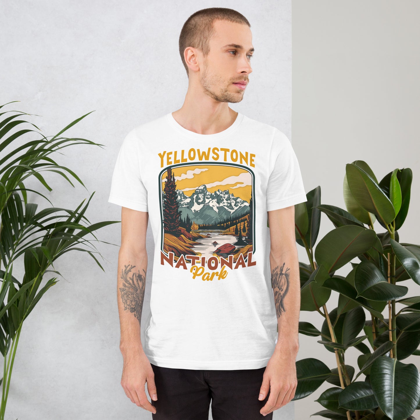 A male with head to the right wearing the Yellowstone National Park T-shirt in white against a wall with flowers